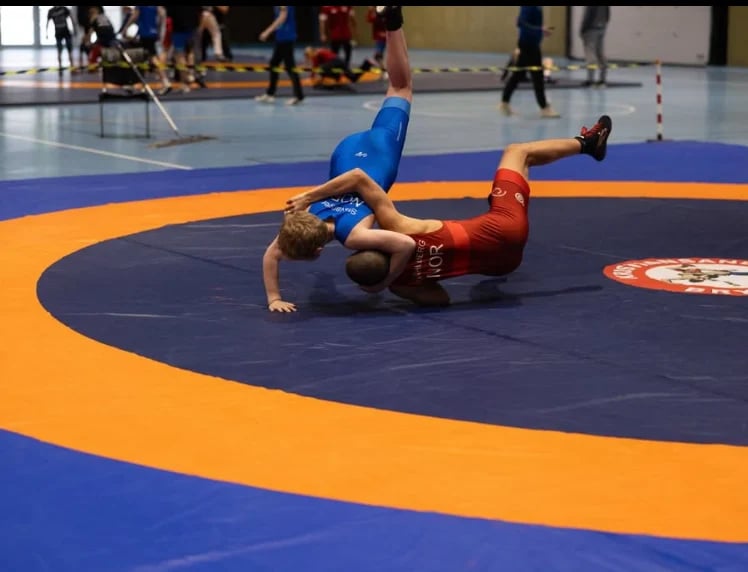 Young wrestler in blue shirt pinning opponent in red on a mat during wrestling competition
