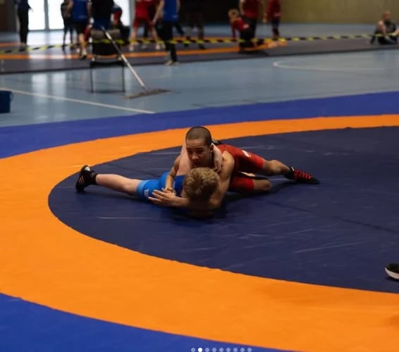 Wrestler performing a takedown move on an opponent on a blue and orange mat during a wrestling match