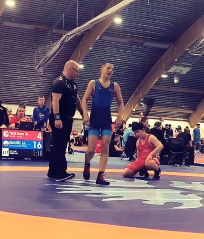 Young wrestlers competing in a tournament on a mat with referee and coach supervising